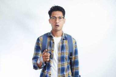 Sırt çantası gözlüklü kızgın Asyalı genç bir öğrenci beyaz arka planda izole edilmiş kamerayı işaret ediyor. Lise üniversite konsepti