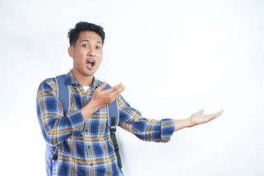 Neşeli Asyalı erkek öğrenci günlük kıyafetler ve sırt çantası gözlükleriyle beyaz arka planda izole edilmiş boş alanı işaret ediyor. Lise üniversite konsepti