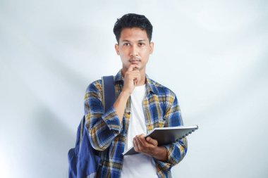 Sırt çantalı genç Asyalı öğrenciler ellerinde defterlerle beyaz arka planda izole edilmiş bir şeyi düşünüyorlar. Lise üniversite konsepti eğitimi