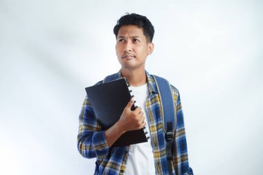 Sırt çantalı, tişörtlü, elinde not defteri olan Asyalı genç bir öğrencinin portresi beyaz arka planda izole edilmiş testi düşünüyor. Lise üniversite konsepti eğitimi