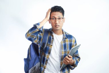 Sırt çantası gözlüklü, kitap tutan ve beyaz arka planda izole edilmiş alnına dokunan üzgün Asyalı genç bir öğrenci. Lise üniversite konsepti eğitimi