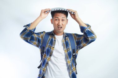 Ders çalışırken stresli ve yorgun hissediyorum. Sırt çantalı genç Asyalı öğrenciler beyaz arka planda izole edilmiş kitapları kafalarında tutuyorlar. Lise üniversite konsepti eğitimi