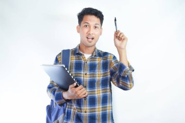 Heyecanlı genç Asyalı erkek öğrenci, günlük giysiler içinde elinde kitap ve kalemle beyaz arka planda izole edilmiş harika bir fikirle işaret ediyor. Lise üniversite konsepti eğitimi