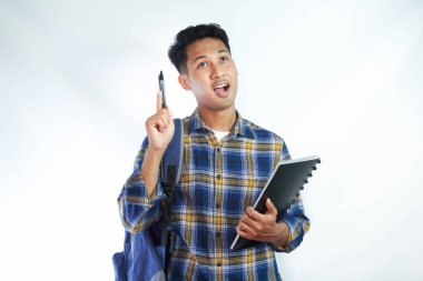 Heyecanlı genç Asyalı erkek öğrenci, günlük giysiler içinde elinde kitap ve kalemle beyaz arka planda izole edilmiş harika bir fikirle işaret ediyor. Lise üniversite konsepti eğitimi