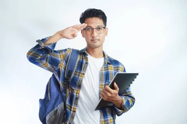 young student man greeting the camera with a military salute in an act of honor and patriotism, showing respect white background