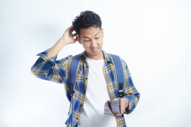 Beyaz arka planda cüzdanını açarken sırt çantalı, şaşırmış ve üzgün bir ifadeyle Asyalı genç bir erkek öğrencinin portresi. Lise üniversite konsepti eğitimi