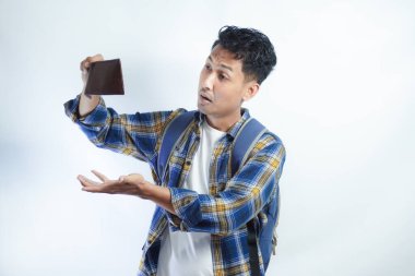 Beyaz arka planda cüzdanını açarken sırt çantalı, şaşırmış ve üzgün bir ifadeyle Asyalı genç bir erkek öğrencinin portresi. Lise üniversite konsepti eğitimi