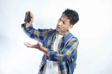 Beyaz arka planda cüzdanını açarken sırt çantalı, şaşırmış ve üzgün bir ifadeyle Asyalı genç bir erkek öğrencinin portresi. Lise üniversite konsepti eğitimi