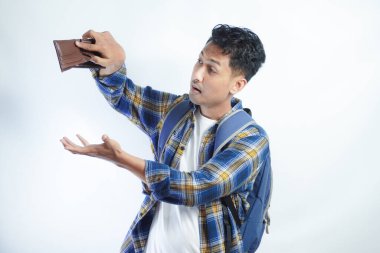 Beyaz arka planda cüzdanını açarken sırt çantalı, şaşırmış ve üzgün bir ifadeyle Asyalı genç bir erkek öğrencinin portresi. Lise üniversite konsepti eğitimi