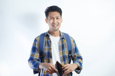 Beyaz arka planda cüzdanını açarken sırt çantalı, şaşırmış ve üzgün bir ifadeyle Asyalı genç bir erkek öğrencinin portresi. Lise üniversite konsepti eğitimi