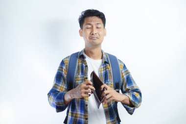 Beyaz arka planda cüzdanını açarken sırt çantalı, şaşırmış ve üzgün bir ifadeyle Asyalı genç bir erkek öğrencinin portresi. Lise üniversite konsepti eğitimi