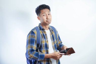 Beyaz arka planda cüzdanını açarken sırt çantalı, şaşırmış ve üzgün bir ifadeyle Asyalı genç bir erkek öğrencinin portresi. Lise üniversite konsepti eğitimi