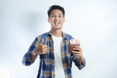 Sırt çantasında beyaz arka planda izole edilmiş para dolu cüzdan taşıyan sıradan giyinmiş gülümseyen Asyalı genç bir öğrenci. Lise Üniversite Konsepti Eğitimi