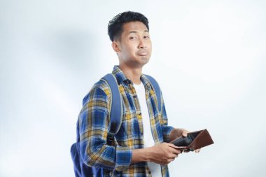 Beyaz arka planda cüzdanını açarken sırt çantalı, şaşırmış ve üzgün bir ifadeyle Asyalı genç bir erkek öğrencinin portresi. Lise üniversite konsepti eğitimi
