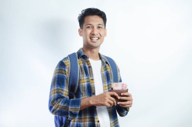 Sırt çantasında beyaz arka planda izole edilmiş para dolu cüzdan taşıyan sıradan giyinmiş gülümseyen Asyalı genç bir öğrenci. Lise Üniversite Konsepti Eğitimi