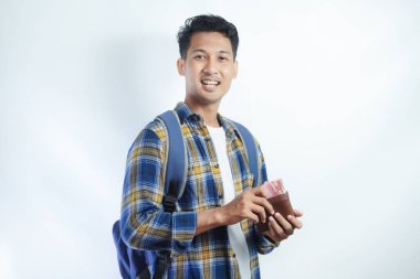 Sırt çantasında beyaz arka planda izole edilmiş para dolu cüzdan taşıyan sıradan giyinmiş gülümseyen Asyalı genç bir öğrenci. Lise Üniversite Konsepti Eğitimi