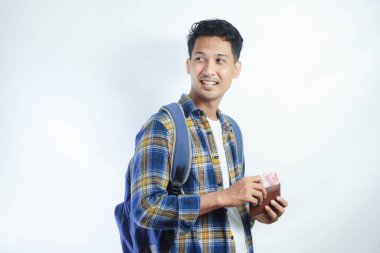 Sırt çantasında beyaz arka planda izole edilmiş para dolu cüzdan taşıyan sıradan giyinmiş gülümseyen Asyalı genç bir öğrenci. Lise Üniversite Konsepti Eğitimi