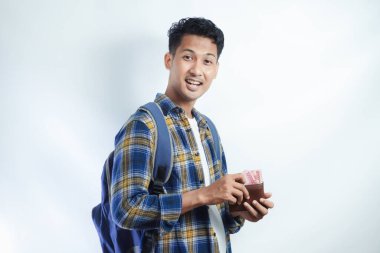 Sırt çantasında beyaz arka planda izole edilmiş para dolu cüzdan taşıyan sıradan giyinmiş gülümseyen Asyalı genç bir öğrenci. Lise Üniversite Konsepti Eğitimi