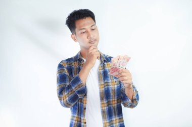 Sırt çantalı dalgın Asyalı genç öğrenci Rupiah banknotlarındaki nakit para hayranı beyaz arka planda izole edilmiş. Lise üniversite konsepti