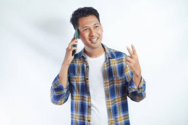 Sırt çantalı, okul kitaplarını tutan ve beyaz arka planda izole bir şekilde cep telefonuyla konuşan neşeli Asyalı genç bir öğrenci. Lise üniversite konsepti eğitimi