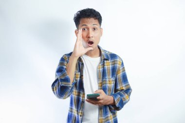 Flanel gömlekli yakışıklı genç adam bağırıyor ve yüksek sesle bağırıyor. Ağzı ağızda ve diğer elinde cep telefonu var. iletişim konsepti.