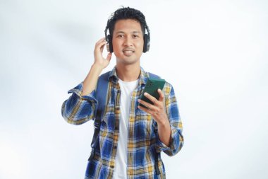 Beyaz arka planda izole edilmiş cep telefonuyla müzik dinlemek için teknoloji kablosuz kulaklık takan rahat Asyalı genç adam. İnsanlar yaşam tarzı kavramını hisseder
