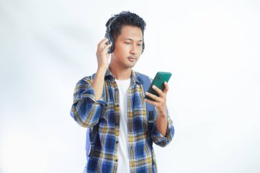 Beyaz arka planda izole edilmiş cep telefonuyla müzik dinlemek için teknoloji kablosuz kulaklık takan rahat Asyalı genç adam. İnsanlar yaşam tarzı kavramını hisseder