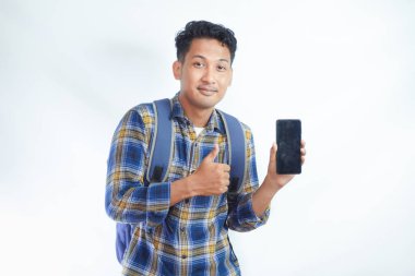 Sırt çantalı neşeli Asyalı genç erkek öğrenci boş ekran akıllı telefonu gösteriyor, el hareketi yapıyor, beyaz arka planda izole edilmiş yeni bir uygulama öneriyor. Lise üniversite konsepti