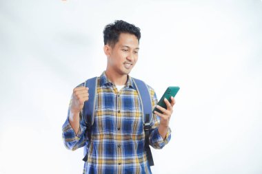 Sırt çantalı, cep telefonlu, heyecanlı Asyalı genç bir öğrenci beyaz arka planda izole edilmiş başarıyı kutluyor. Lise üniversite konsepti