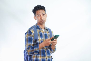 Mutsuz genç Asyalı erkek öğrenci sırt çantasıyla ayakta cep telefonu kullanarak beyaz arka planda izole bir şekilde sohbet ediyor. Lise üniversite konsepti