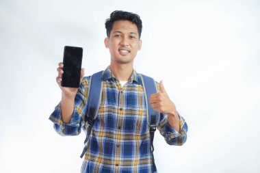 Sırt çantalı neşeli Asyalı genç erkek öğrenci boş ekran akıllı telefonu gösteriyor, el hareketi yapıyor, beyaz arka planda izole edilmiş yeni bir uygulama öneriyor. Lise üniversite konsepti