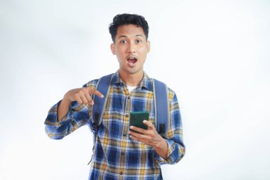 Rahat kıyafetler ve sırt çantalı genç Asyalı öğrenci cep telefonunu işaret ederek beyaz arka planda izole edilmiş bir uygulama öneriyor. Lise üniversite konsepti
