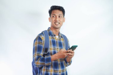 Sırt çantasıyla gülümseyen Asyalı genç bir öğrenci beyaz arka planda cep telefonunu elinde tutarken ayakta duruyor. Lise üniversite konsepti
