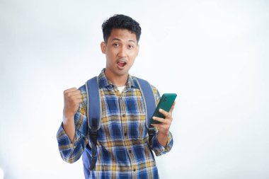 Sırt çantalı, cep telefonlu, heyecanlı Asyalı genç bir öğrenci beyaz arka planda izole edilmiş başarıyı kutluyor. Lise üniversite konsepti