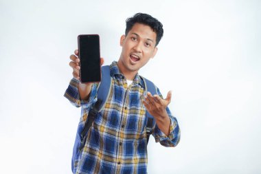 Gündelik giysiler içinde neşeli Asyalı genç bir erkek öğrenci ve sırt çantalı gözlüklerle cep telefonunu boş ekran ile işaret ederek beyaz arka planda izole edilmiş uygulamayı tavsiye ediyor. Lise üniversite konsepti