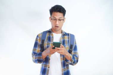 Sırt çantası gözlüklü, cep telefonu kullanan, internette sohbet eden ve beyaz arka planda izole edilmiş haberleri okuyan Asyalı bir öğrenci. Lise üniversite konsepti