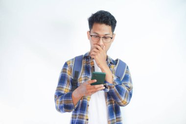 Sırt çantası gözlüklü, cep telefonu kullanan, internette sohbet eden ve beyaz arka planda izole edilmiş haberleri okuyan Asyalı bir öğrenci. Lise üniversite konsepti