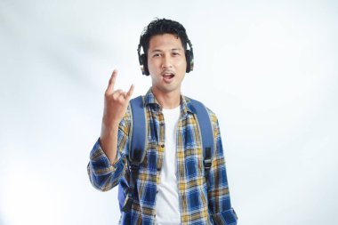 Rock 'n Roll. Sırt çantalı yakışıklı Asyalı genç bir öğrenci, kulaklıklı rock müzik dinliyor ve beyaza izole edilmiş metal rock hareketleri gösteriyor. Eğitim Fakültesi