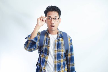 Beyaz arka planda izole edilmiş kameraya bakarken sırt çantası gözlüklü, heyecanlı ve şaşırmış Asyalı bir genç. Lise üniversite konsepti eğitimi