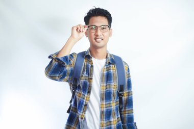 Sıradan kulaklıklar ve sırt çantası takan gülümseyen çekici Asyalı öğrenci kendinden emin bir şekilde beyaz arka planda izole edilmiş kameraya bakıyor. Lise üniversite konsepti