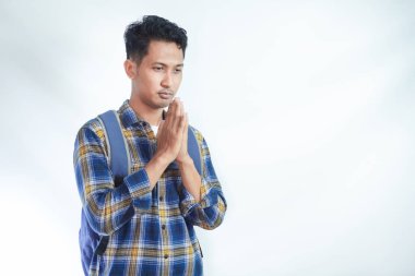 Sırt çantalı, sıradan kıyafetler giyen dindar, genç Asyalı bir öğrenci el çabukluğuyla beyaz arka planda izole edilmiş bir şey için yalvarıyor. Lise üniversite konsepti