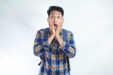 20 'li yaşlarda, sıradan kıyafetler giyen, sırt çantalı, elinde yanağıyla beyaz arka plandaki kameraya bakan genç bir Asyalı. Lise üniversite konsepti