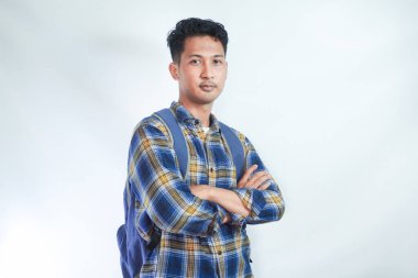 Sırt çantası katlanmış günlük kıyafetler giyen ve beyaz arka planda izole edilmiş kameraya bakan kendine güvenen Asyalı genç bir öğrenci. Lise üniversite konsepti