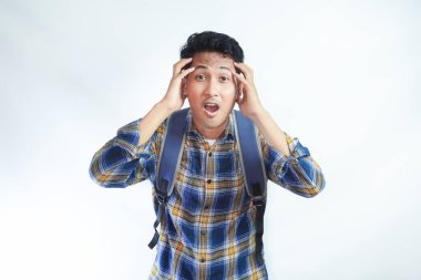 Sırt çantalı Asyalı genç bir öğrenci ellerini beyaz arka planda izole bir şekilde başının üstüne koydu. Lise üniversite konsepti