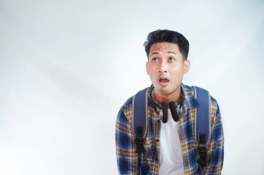 Sırt çantası gözlüklü heyecanlı Asyalı genç bir öğrenci beyaz arka planda izole edilmiş çalışma alanı modeline bakıyor. Lise üniversite konsepti eğitimi