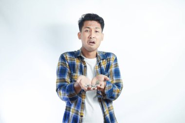 Flanel tişört giyen Asyalı genç adam elinde üzgün ifadeli birkaç bozuk para tutuyor. Zavallı adam konsepti