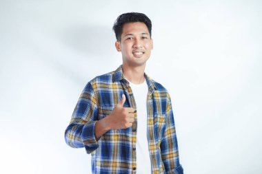 Yetişkin Asyalı adam gülümsüyor ve kameraya başparmağını uzatıyor.