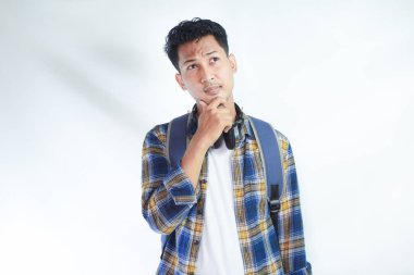 Sırt çantasıyla tişört giyen ve beyaz arka planda izole edilmiş testi düşünen dalgın Asyalı genç bir öğrencinin portresi. Lise üniversite konsepti eğitimi