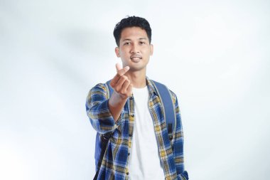 Sırt çantasıyla kolejden gülümseyen Asyalı genç bir erkek öğrenci, Koreli bir kalp işareti gösteriyor, beyaz arka planda izole edilmiş size aşkı ifade ediyor.