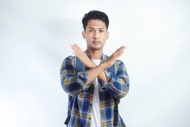 Sırt çantalı Asyalı genç bir öğrenci beyaz arka planda çapraz el hareketleriyle durduğunu gösteriyor. Lise üniversite konsepti